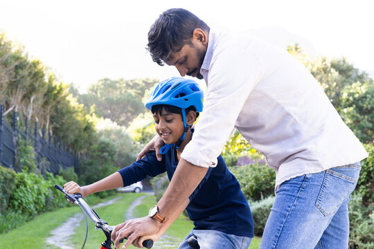 indian father teaching young son to ride bicycle, bonding outdoors in nature