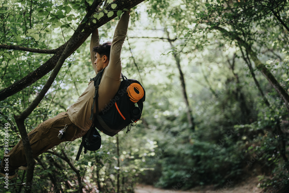 Wall mural Young man climbing a tree branch during a forest hike. Emphasizes adventure, outdoor fitness, and the natural environment.