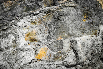 Close-up of a weathered rock with a rough, textured surface. The stone displays varied shades, from light to dark patches, revealing natural erosion details