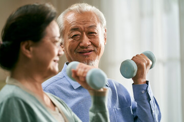 happy senior asian couple exercising at home using dumbbells