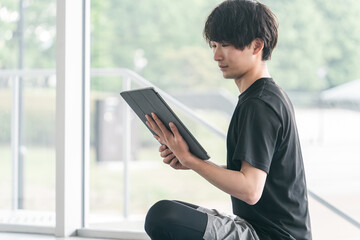 タブレット端末を使うスポーツウェア姿の若いアジア人男性
