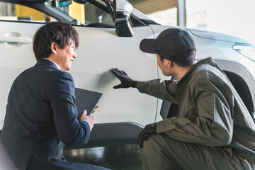 車の傷・凹みを確認する整備士の男性とスーツ姿のセールスマン

