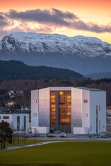 Fototapeta premium A modern building set against a snowy mountain backdrop during sunset.