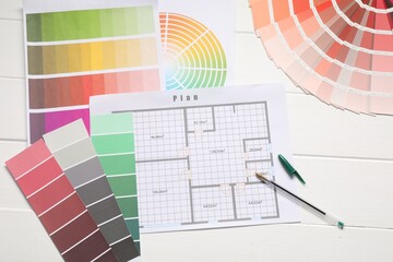 Designer's workplace with color palettes, floor plan and pen on white wooden table, flat lay