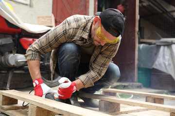 Man grinding wooden planks with angle grinder outdoors