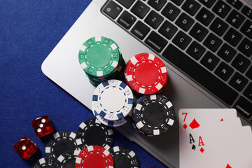 Poker chips, laptop, playing cards and dices on blue table, flat lay. Online game © New Africa