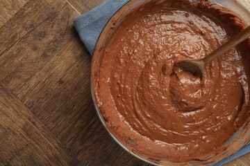 Chocolate dough in bowl and spoon on wooden table, top view. Space for text