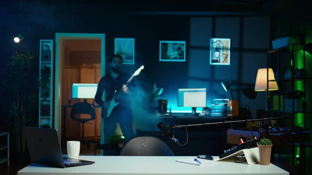 Playful internet star playing guitar in studio while shooting video. Energetic content creator playing musical instrument while filming vlog with professional mic in home studio, camera B