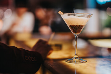 Close-up of a stylish cocktail glass on a bar counter, capturing the essence of a lively night out with blurred background ambiance.