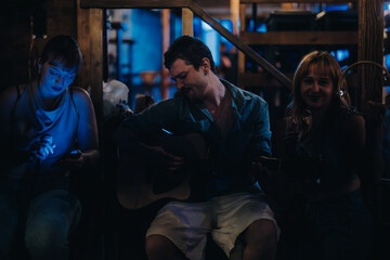 A group of young musicians performing together in a cozy, dimly lit venue, featuring a guitarist, singer, and tambourine player, capturing a relaxed and intimate musical atmosphere.