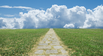 緑の野原を貫く遠く地平線へ続く石畳の一本道　背景の青空と雲　アウトドア・夏・遠足・スタート・はじまりのイメージ背景