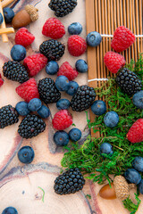 Close-up of fresh blueberry, raspberry, and blackberry with green moss on wooden background. Selective focus.