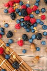 Close-up on mix berries: blackberries, blueberries, raspberries and acorns isolated on a wooden table background, vertical image