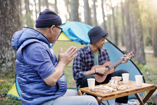 Happy father and son enjoying camping day while boy playing acoustic guitar at campsite