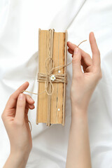 Books with flowers wrapped in burlap thread on a light background.