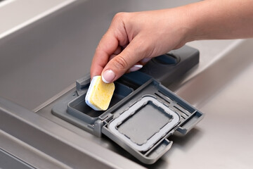 female hand puts dishwasher tablet into open automatic built-in dishwasher machine. Close up