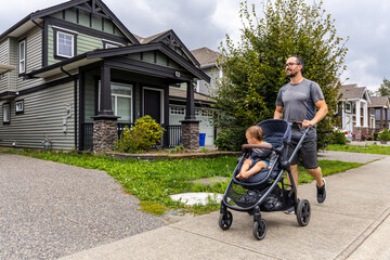 Father Enjoying a Stroll with Toddler in Stroller Through Residential Neighborhood in Mission, BC,...