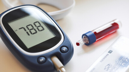 Glucose meter showing a reading of 7.8 with a filled test tube and blood sampling equipment on a white surface.