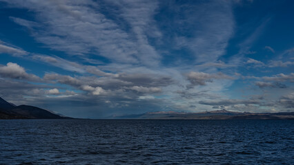 Obraz premium Beautiful seascape. Ripples on the surface of the blue ocean. Mountains and coastline are visible in the distance. Picturesque clouds in the sky. Argentina. The Beagle Channel. Tierra del Fuego