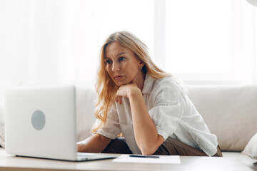 Woman sitting on a couch with a laptop, looking at the camera, in a cozy living room setting