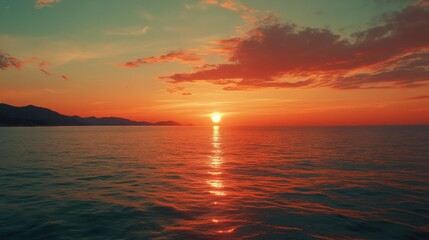 Obraz premium Stunning sunset over a tranquil ocean with silhouettes of distant mountains reflecting warm hues during twilight