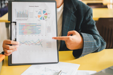 A business professional in a suit presenting a financial summary report with various charts and graphs in an office environment.