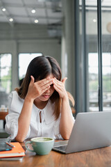 A young woman experiencing stress while working on her laptop in a modern cafe, with coffee and...