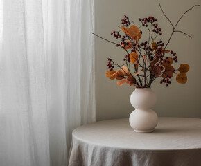 A vase with autumn leaves bouquet on a round table with a linen tablecloth in the living room