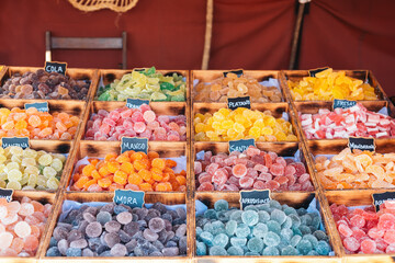 A colorful display of various types of sugar-coated gummy candies in wooden boxes at a fair in Galicia, Spain.