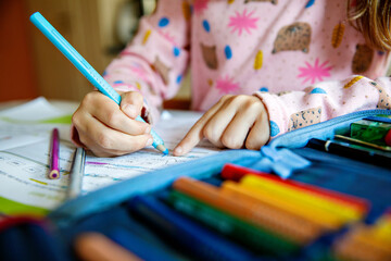Naklejka premium Little girl making school homework. Cute child with eyeglasses learning at home, writing with pencils in workbook.