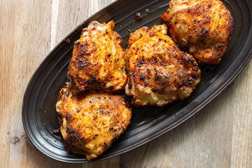 Fried chicken with hot thai bbq seasoning on a black stoneware dish. On wooden background