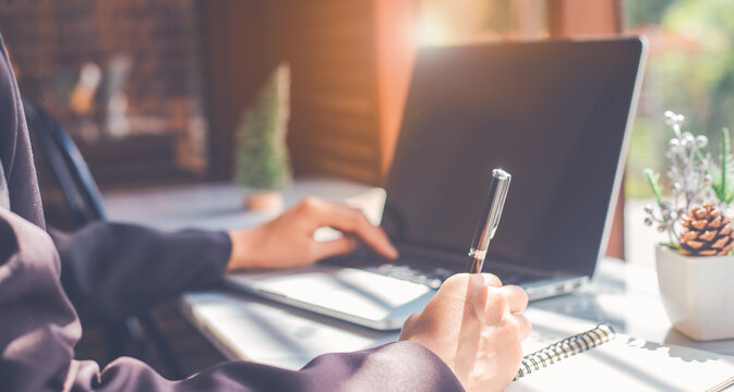 Woman hand writing on a notepad with a pen and use a laptop computer in the office.For web banner.