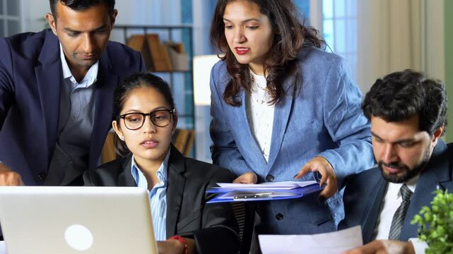 A young Indian team of professionals or businessmen working together looking over project documents and showing slight disappointment with the results while discussing how to make things better