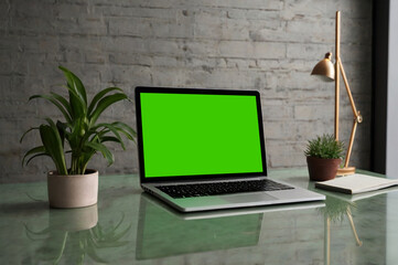 Sleek laptop with green screen on clean surface, ideal for chroma key, soft natural lighting.