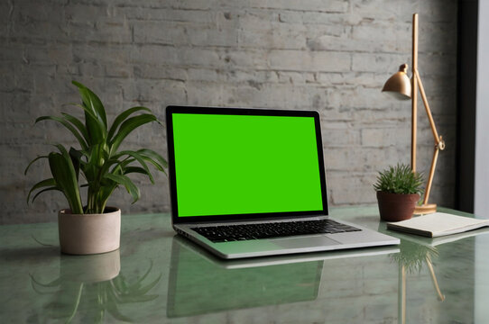 Sleek laptop with green screen on clean surface, ideal for chroma key, soft natural lighting.