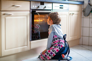 Cute blond boy baking muffins or pie in domestic kitchen. Happy child having fun with helping,...