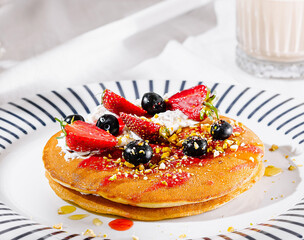 Delicious pancakes topped with strawberries, blueberries and pistachios on white plate