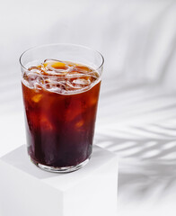 Cold brew coffee standing on white cube with tropical plant shadow