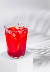 Refreshing red cocktail standing on white cube with tropical palm leaf shadow