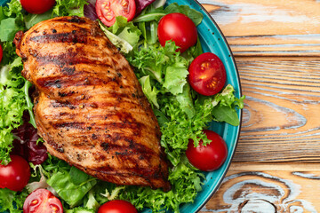 Grilled chicken breast ( fillet ) with lattuce salad and cherry tomatoes . Top view