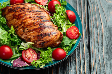 Grilled chicken breast ( fillet ) with lattuce salad and cherry tomatoes . Top view