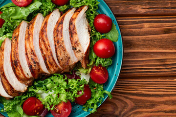 Grilled chicken breast ( fillet ) with lattuce salad and cherry tomatoes . Top view