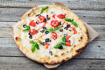 Pizza with mozzarella cheese , olives , chicken , pineapple , basil and tomatoes