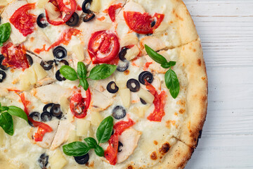 Pizza with mozzarella cheese , olives , chicken , pineapple , basil and tomatoes