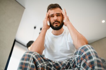 Man suffering from headache at home, touching his temples, copy space, blurred background. Migraine, headache, stress, tension problem, hangover concept