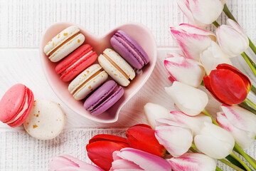 Pastel colorful tulips and vibrant macaroons fill a heart-shaped bowl