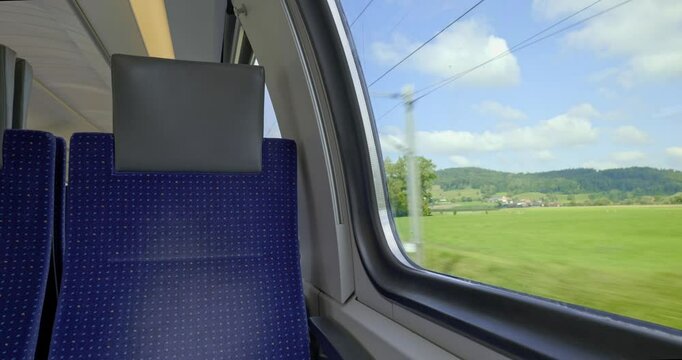 Empty bench seats inside moving public passenger train in Europe. Wide angle view, large windows, green summer nature landscape outside, real time, no people