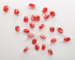 Red caramel candies in transparent wrapper scattered on a white background.