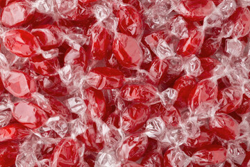 Background of red caramel candies in transparent candy wrappers. Pile of cherry candies.