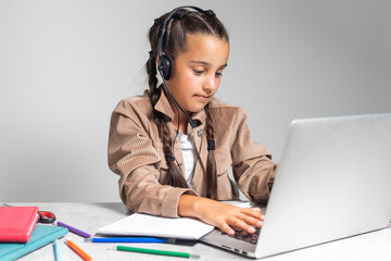 Child online. A little girl uses a laptop video chat to communicate learning while sitting at a table at home.